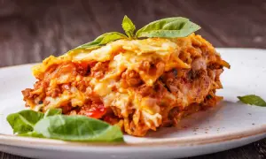 Una fetta di lasagna salentina, ricca e saporita, guarnita con basilico fresco, su un piatto bianco.