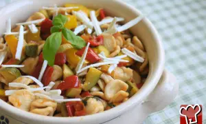 Orecchiette pugliesi con verdure colorate e formaggio grattugiato, guarnite con basilico fresco.