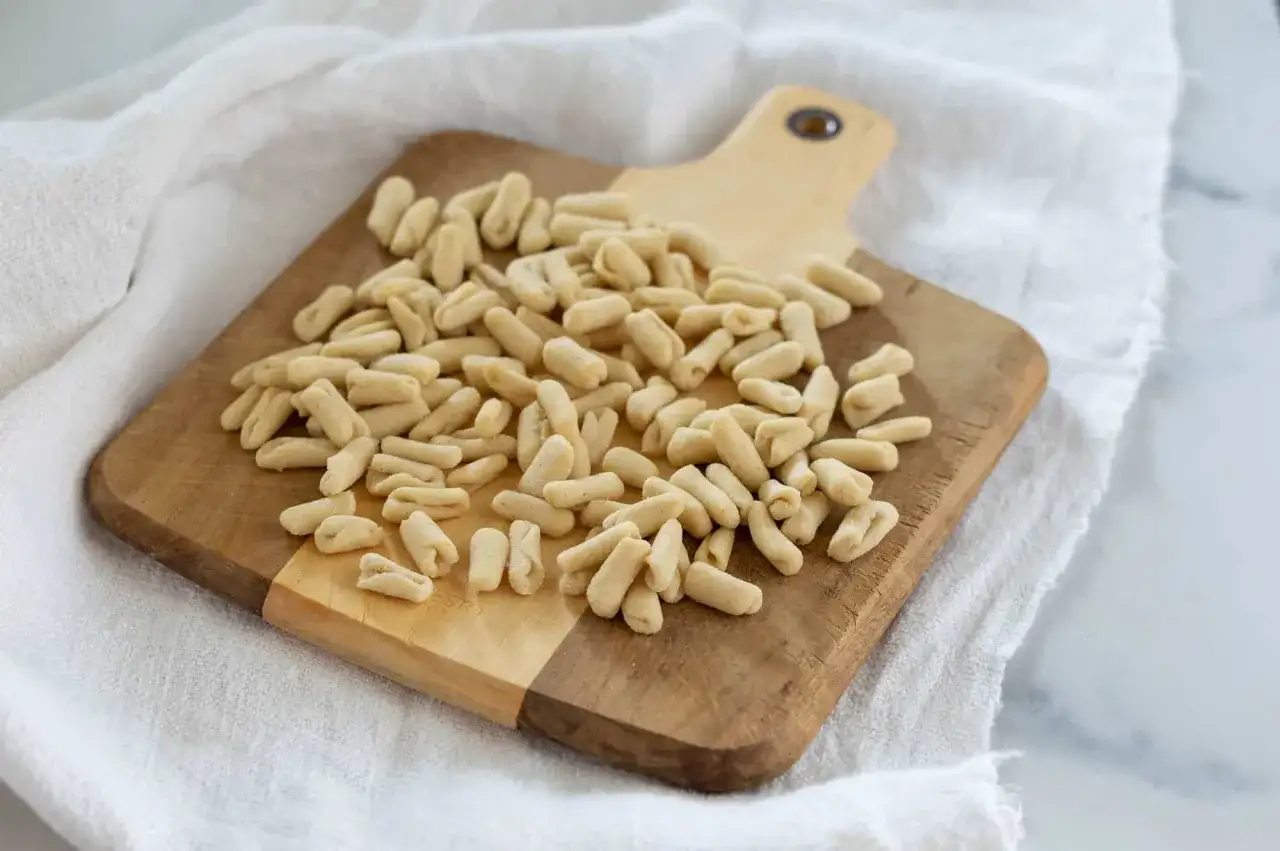 Un mucchio di cavatelli pugliesi freschi su un tagliere di legno, pronti per essere cucinati.