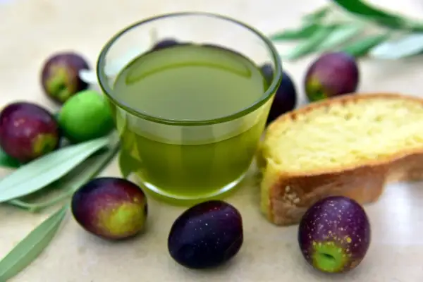 Olio extra vergine d'oliva e olive fresche, eccellenza dei prodotti DOP Puglia, accompagnati da una fetta di pane.