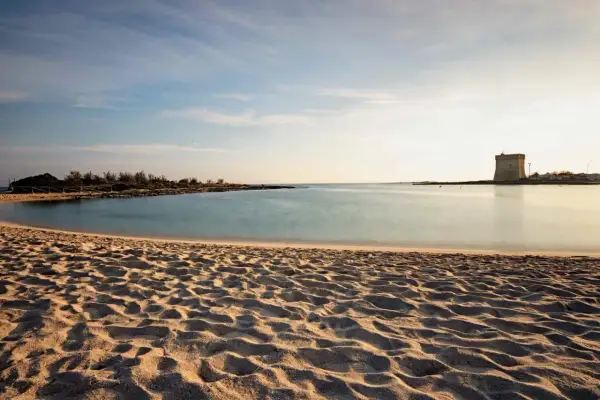 Spiagge Salento Ionico: sabbia dorata, mare calmo e una torre antica all'orizzonte, un sogno ad occhi aperti.