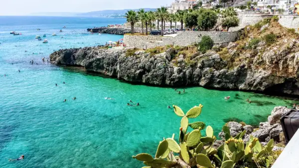 Scogliera con mare cristallino e gente che nuota, tipica dei paesi sul mare in Puglia.