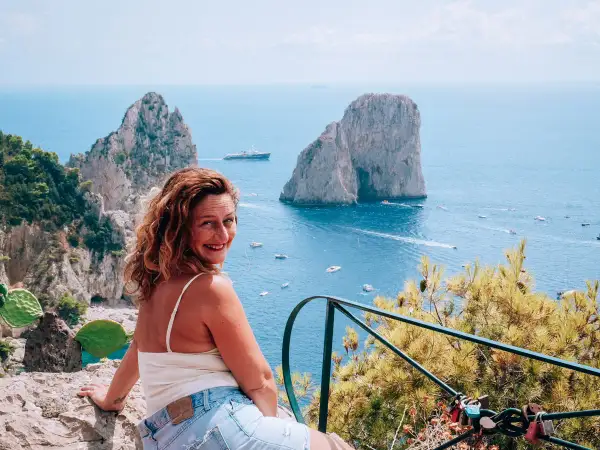 Donna sorridente con vista sui Faraglioni e il mare azzurro, un ricordo dalla spiaggia di Marina Piccola.